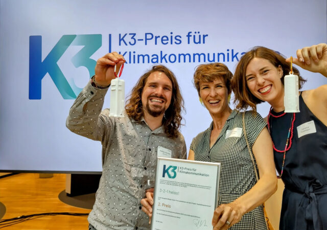 Pia Viviani hält ein Diplom und lacht. Links und rechts von ihr je eine Person, die sich ebenfalls freuen.